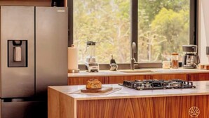 Eine moderne Küche mit einem Edelstahl-Kühlschrank, einem eingebauten Herd und einem großen Fenster mit Blick auf Bäume.