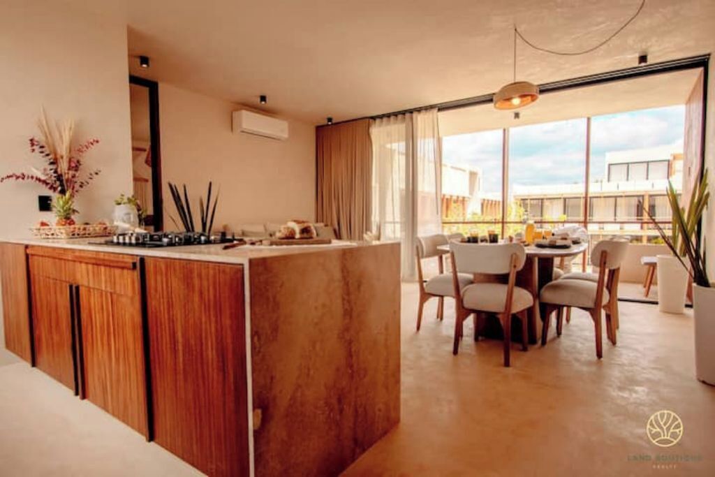 A modern kitchen with a central island, dining area with chairs, and large windows offering a view of the city.