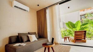 A modern living room with a sofa, a laptop on a small wooden stool, and a large window with curtains. - Spacious high-end apt w/ private pool (Tulum)