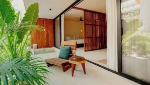 A modern room with a wooden bench, a small round table, and a bed with a green pillow. - Spacious high-end apt w/ private pool (Tulum)