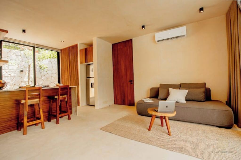 Een moderne woonkamer met een bank, een laptop op een bijzettafeltje, en een eethoek met houten stoelen en een tafel.