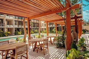 Ein überdachter Außenbereich mit Holzmöbeln und einem Pool im Hintergrund.