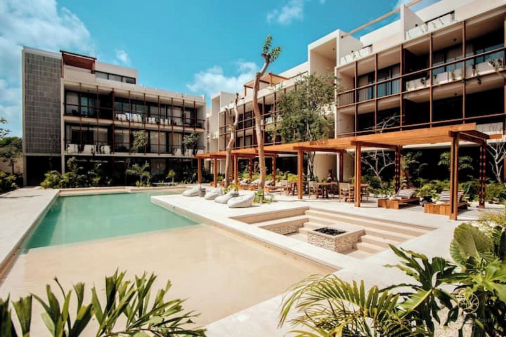 A modern hotel with a swimming pool, outdoor seating, and lush landscaping.