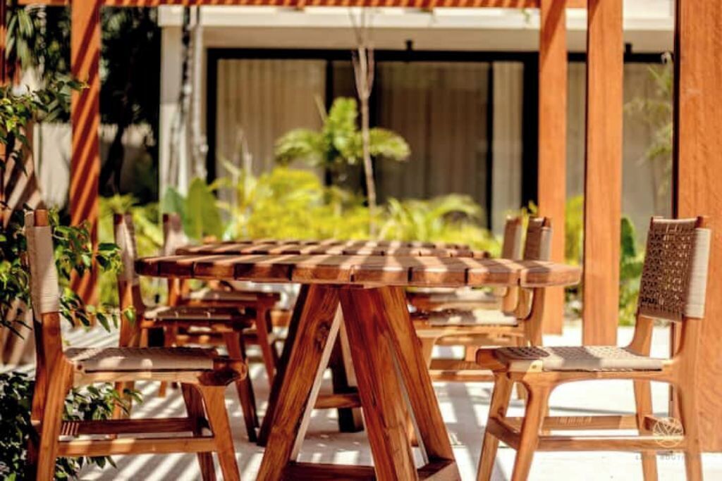 Een houten eethoek buiten, met stoelen en een tafel, omringd door groen.