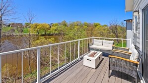 A deck with outdoor furniture, a fire pit, and a view of a river and trees. - Sheboygan Riverside Condo (Sheboygan)