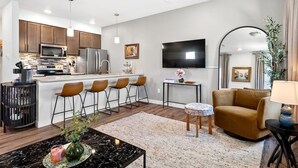 A modern kitchen with a central island, bar stools, and a dining area with a round table and chairs. - Sheboygan Riverside Condo (Sheboygan)