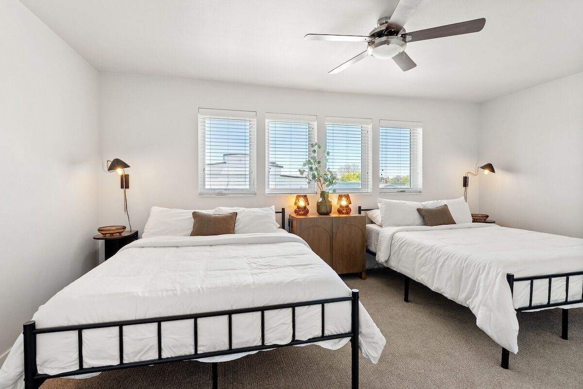 A bedroom with two single beds, a ceiling fan, and a nightstand with a lamp.
