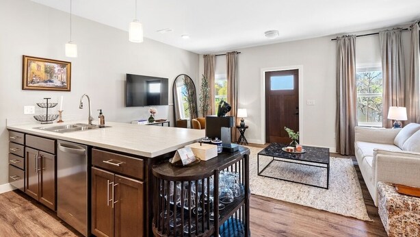A modern kitchen with a central island, a dining area with a coffee table, a sofa, and a TV mounted on the wall. - Sheboygan Riverside Condo (Sheboygan)