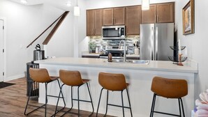 A modern kitchen with wooden cabinets, stainless steel appliances, and a central island with bar stools. - Sheboygan Riverside Condo (Sheboygan)