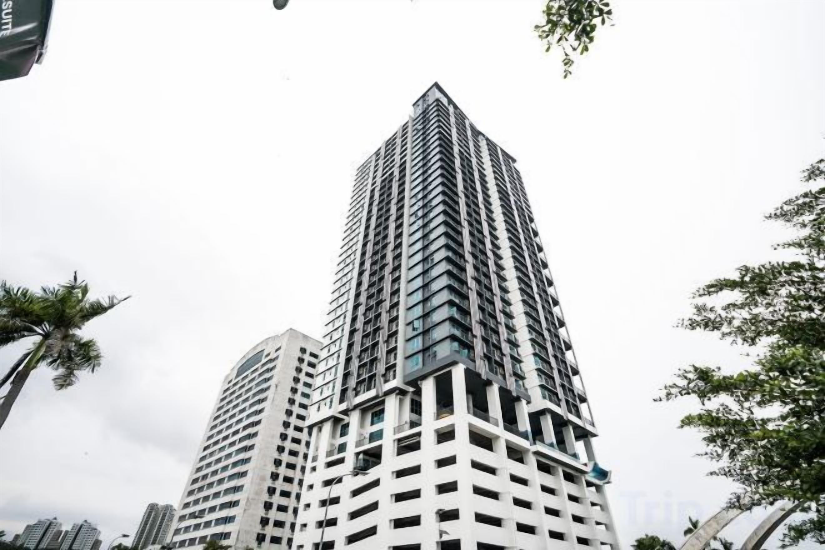 A tall, modern building with a grid-like facade, surrounded by palm trees and other greenery.