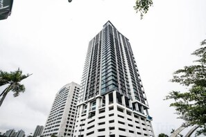 Un edificio alto y moderno con fachada de diseño geométrico, rodeado de palmeras y otra vegetación.