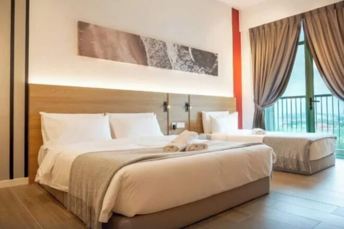 A hotel room with a large bed, a smaller bed, a balcony with curtains, and a painting on the wall.