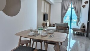 A modern dining area with a wooden table set for four, a sofa, and a TV mounted on the wall. - Liwan, Baysuite by Ayuhouz (Kota Kinabalu)