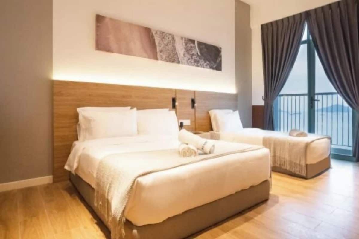 A double bed with a wooden headboard, a bedside table, and a view of the outdoors through large windows.