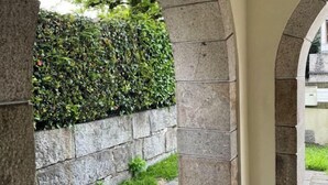 Ein steinernes Torbogen führt zu einer Steinmauer mit einer Hecke.