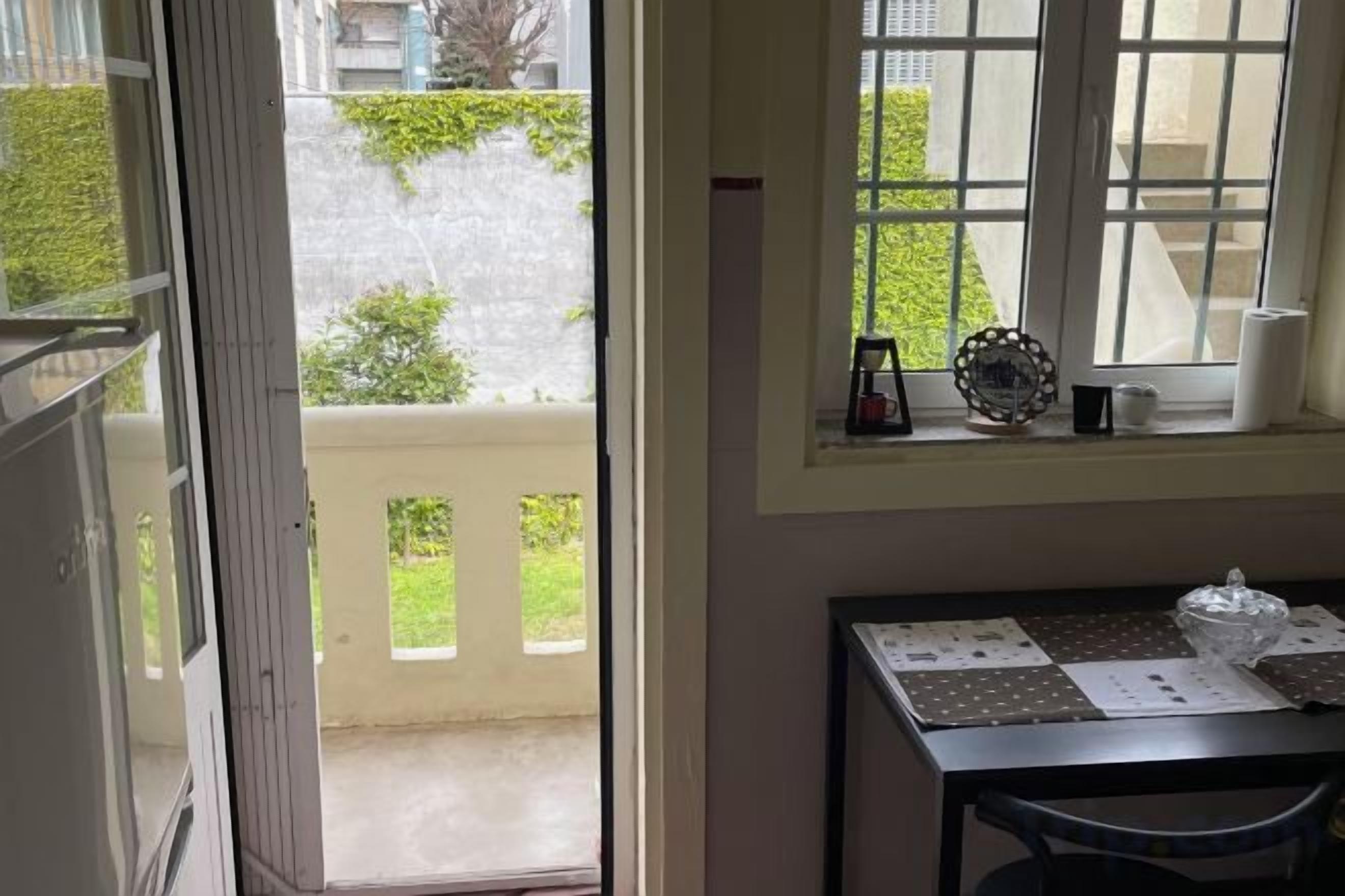 A room with a table, a window with a view of the street, and a door leading outside.