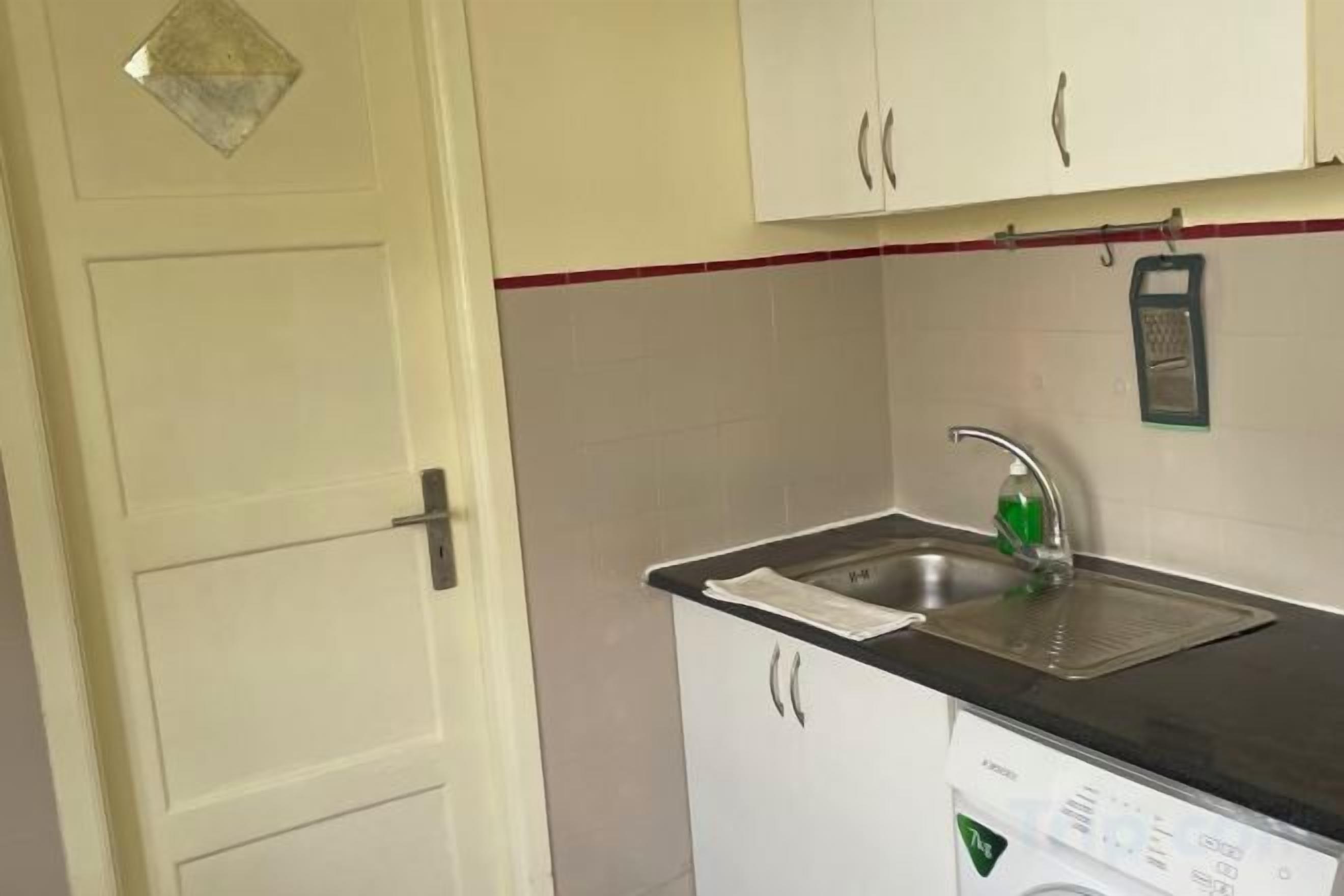 Cocina compacta con lavabo, lavadora y armarios.