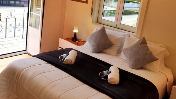 Ein Hotelzimmer mit Bett, Kissen, einem Nachttisch mit Lampe und einem Fenster.