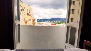 Ein Zimmer mit Bett, Fenster und Blick auf Gebäude und Hügel.