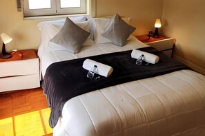 Una cama bien hecha con almohadas, una mesita de noche con lámpara y una ventana.