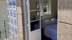 Ein Zimmer mit Bett, einem Fenster mit Jalousien und einer Tür zu einem Außenbereich.