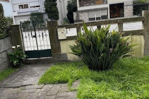 Ein begrenzter Eingang mit einer Betonmauer, einem Metallgitter und einer kleinen grünen Pflanze im Vordergrund.