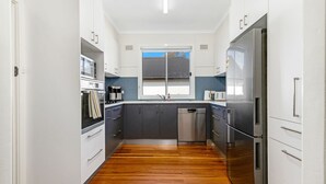 A compact kitchen with white cabinets, a stainless steel refrigerator, a dishwasher, and a window above the sink. - Beachfront Escape Relaxing Getaway in Batehaven (Batehaven)