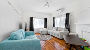 A modern living room with a light blue sofa, a grey sectional sofa, and a small table. There is a fireplace on the right and a ceiling fan. - Beachfront Escape Relaxing Getaway in Batehaven (Batehaven)