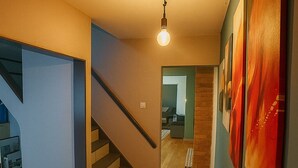 A modern interior with a staircase leading to a second floor, a hallway with artwork, and a visible kitchen area. - Entire luxury home free parking - Discount for long stays and contractors (Birmingham)