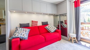 Un salon moderne avec un canapé rouge, des meubles de rangement gris et un petit tabouret.