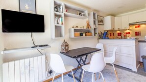 Un espace de vie compact comprenant un téléviseur à écran plat fixé au mur, une table à manger avec des chaises et un coin cuisine.