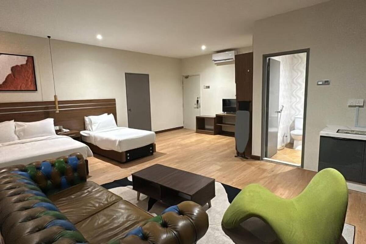A hotel room with a bed, a sofa, a coffee table, a TV, and a bathroom visible through an open door.