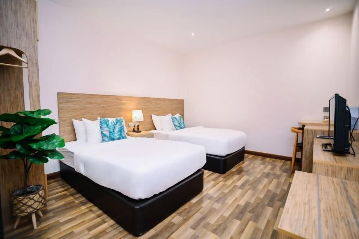 A hotel room with two beds, a desk, a TV, and a large plant.