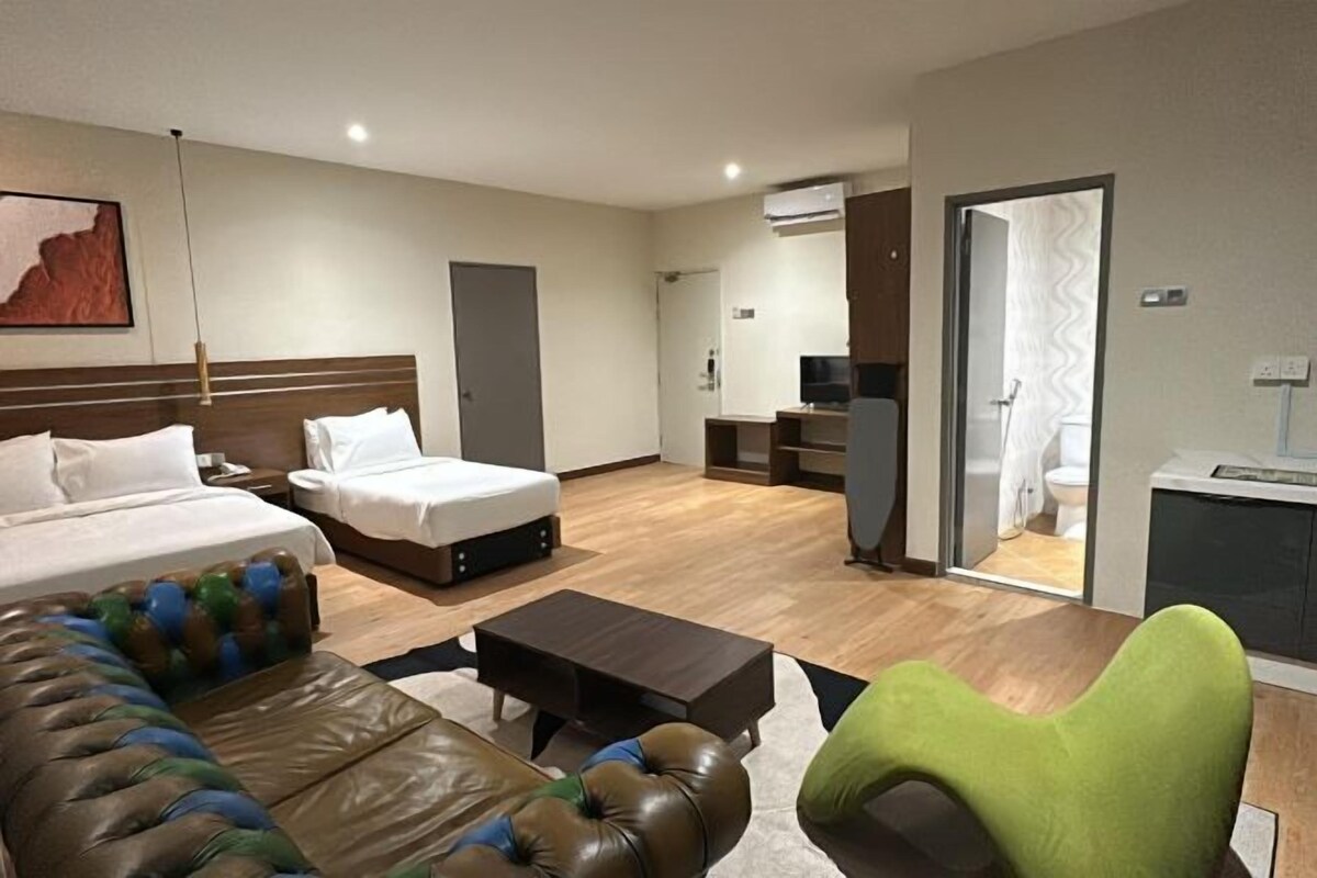 A hotel room with a bed, a sofa, a coffee table, a TV, and a bathroom visible through an open door.