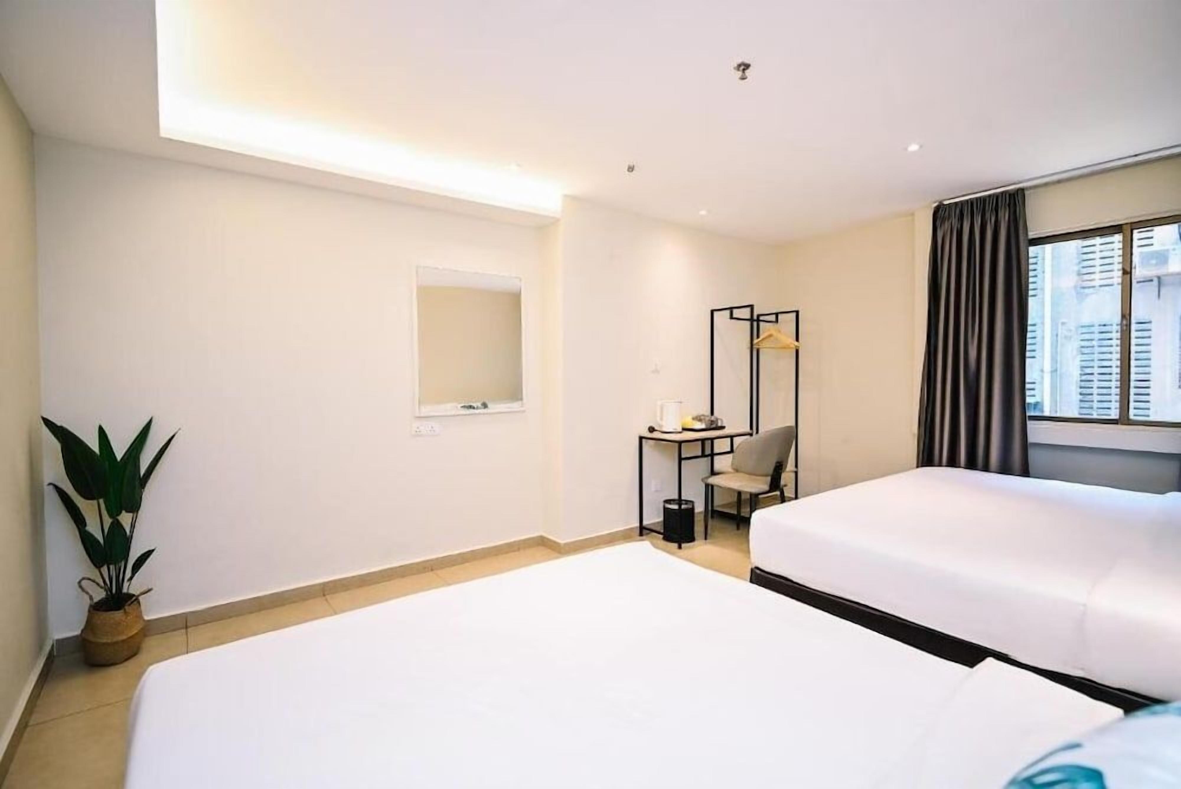 Une chambre d’hôtel avec deux lits, un bureau avec une chaise, un miroir et une plante en pot.