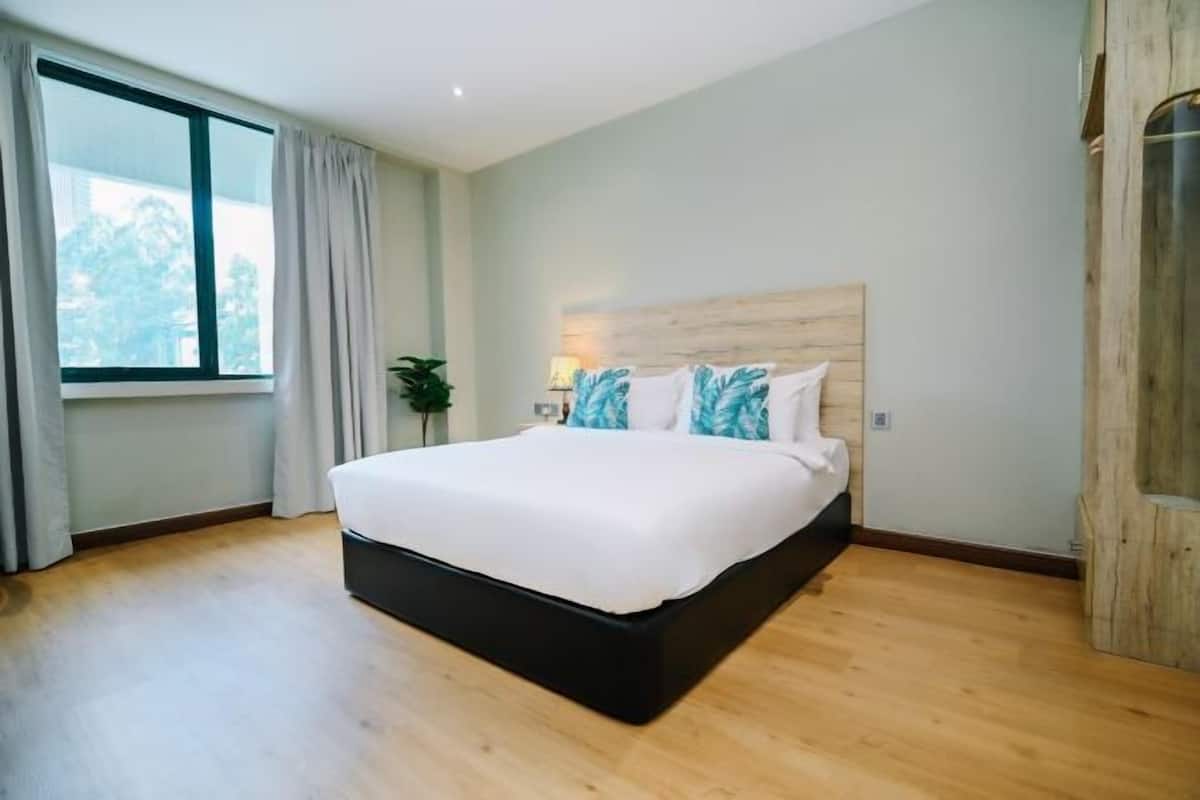 A modern bedroom with a large bed, a wooden headboard, and a view of greenery outside.