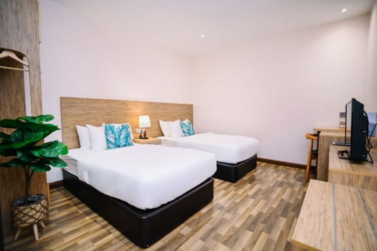 A hotel room with two beds, a desk, a TV, and a large plant.