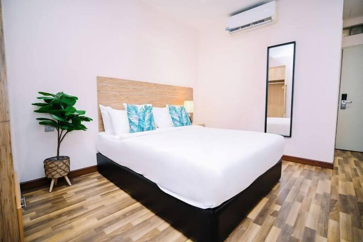 A bedroom with a large bed, a wooden headboard, a potted plant, and a mirror on the wall.