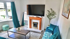 Un salon avec une cheminée, un téléviseur, des meubles de couleur turquoise et une fenêtre avec des rideaux.