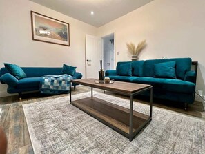 A living room with two teal sofas, a wooden coffee table, and a patterned rug.