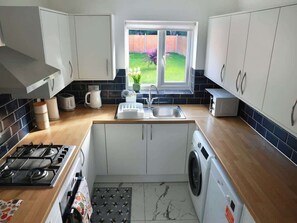 A compact kitchen with a gas stove, sink, and washing machine, a window with a view of a garden, and white cabinets.