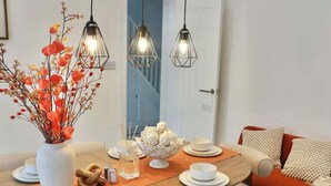 Un coin repas avec une table en bois, des assiettes blanches, un vase avec des branches et un saladier rempli d’artichauts.