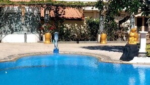 A swimming pool with a statue, surrounded by a stone wall and plants. - Grand Melka Hotel (Bali)