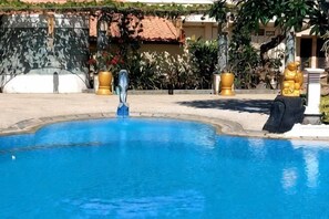 A swimming pool with a statue, surrounded by a stone wall and plants. - Grand Melka Hotel (Bali)