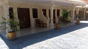 A covered outdoor area with a tiled floor, potted plants, and a wooden door. - Grand Melka Hotel (Bali)