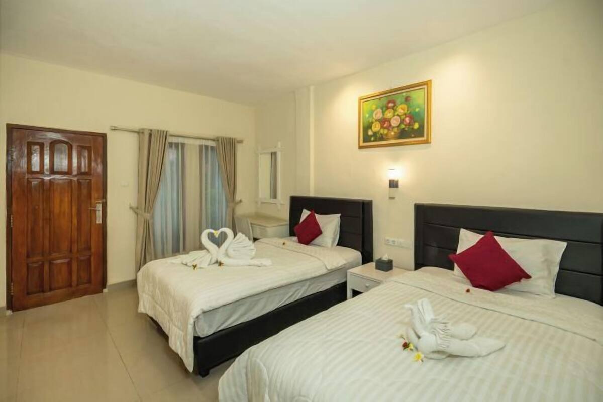A hotel room with two beds, a wooden door, a painting, and a window with curtains.