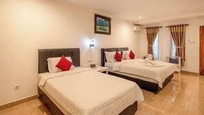 A hotel room with two beds, a nightstand, a wall-mounted lamp, a painting, and a window with curtains. - Grand Melka Hotel (Bali)