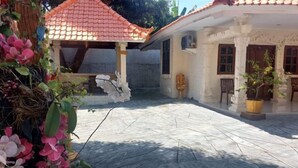 A courtyard with a tiled roof structure, a white building with windows, and potted plants. - Grand Melka Hotel (Bali)
