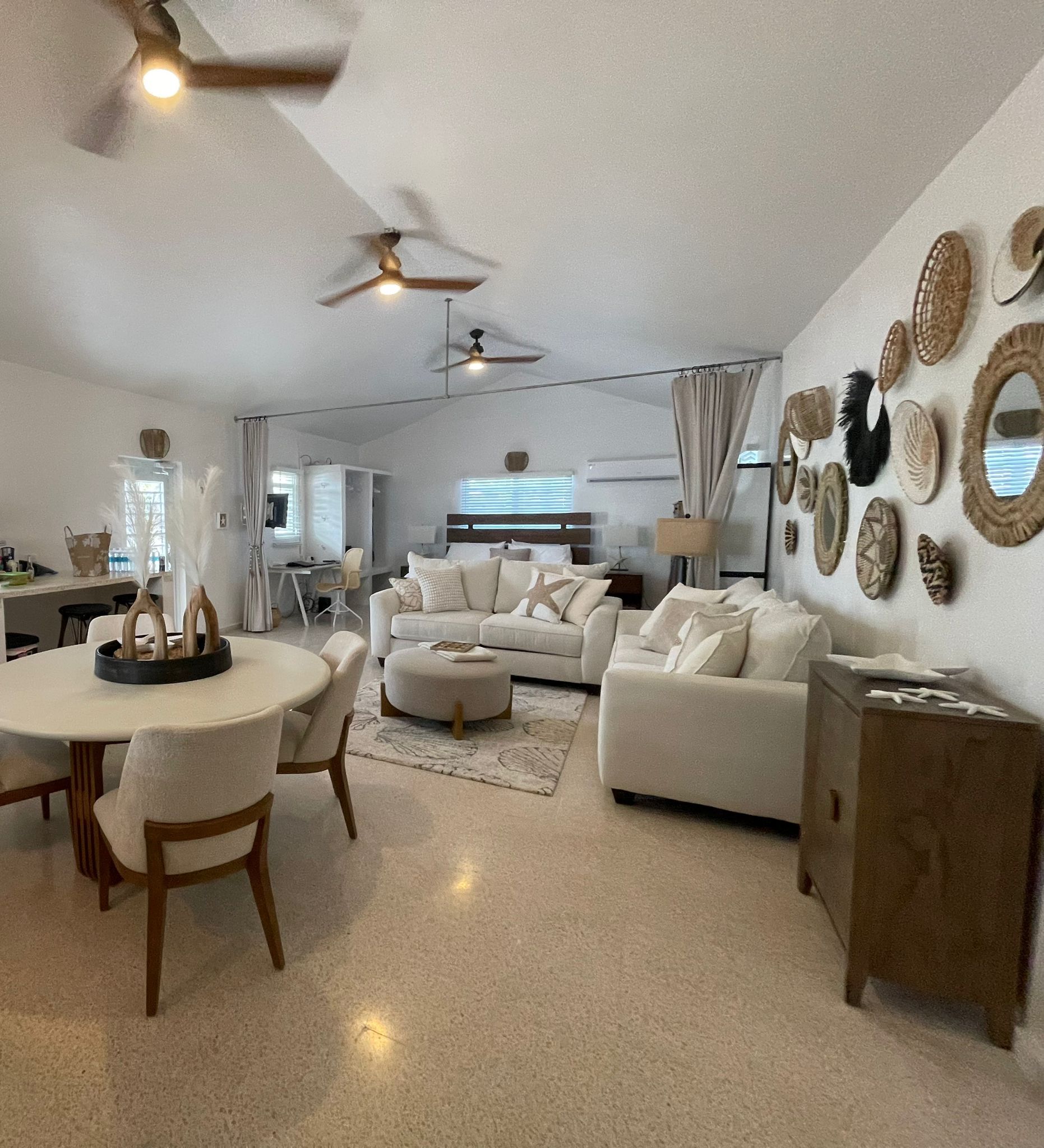 A spacious living room with a white sofa set, a dining area with a round table, and a ceiling fan.