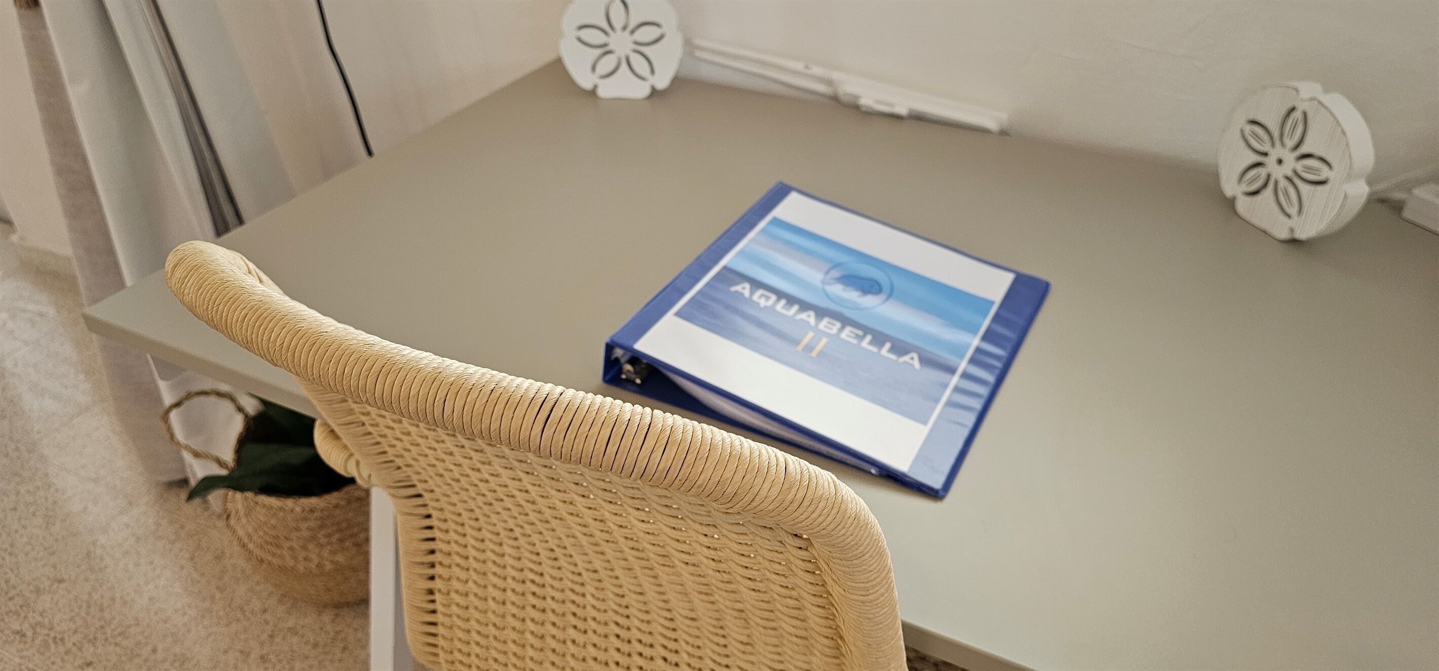 A small table with a blue book titled "Aquabella II" and two decorative white objects with floral designs.